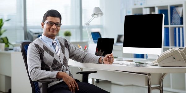Portrait of cheerful Indian manager at his table looking at the camera